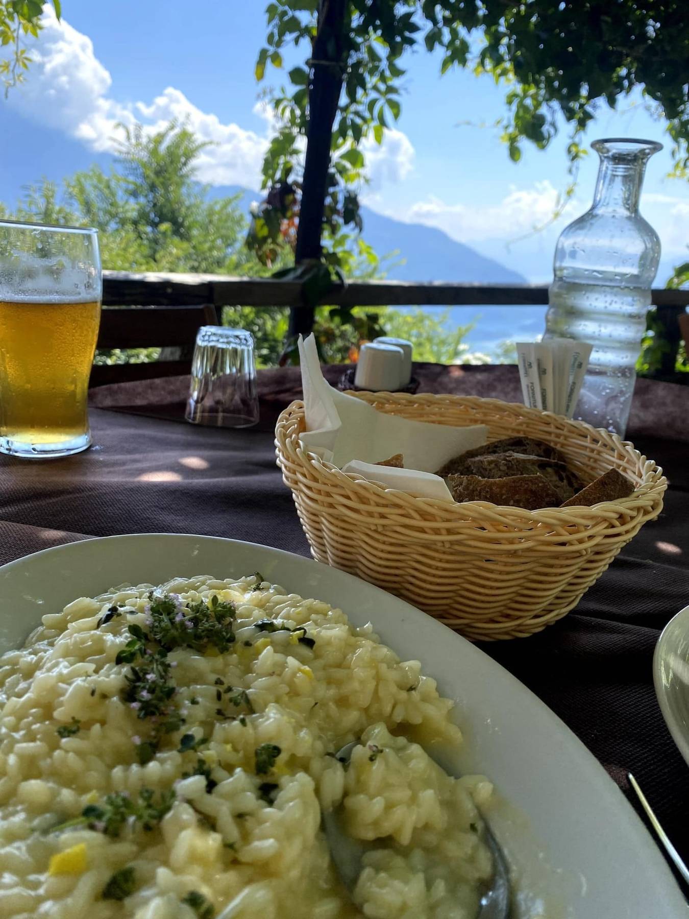 Risotto med timian, brød og et glass øl på et bord med utsikt mot Comosjøen